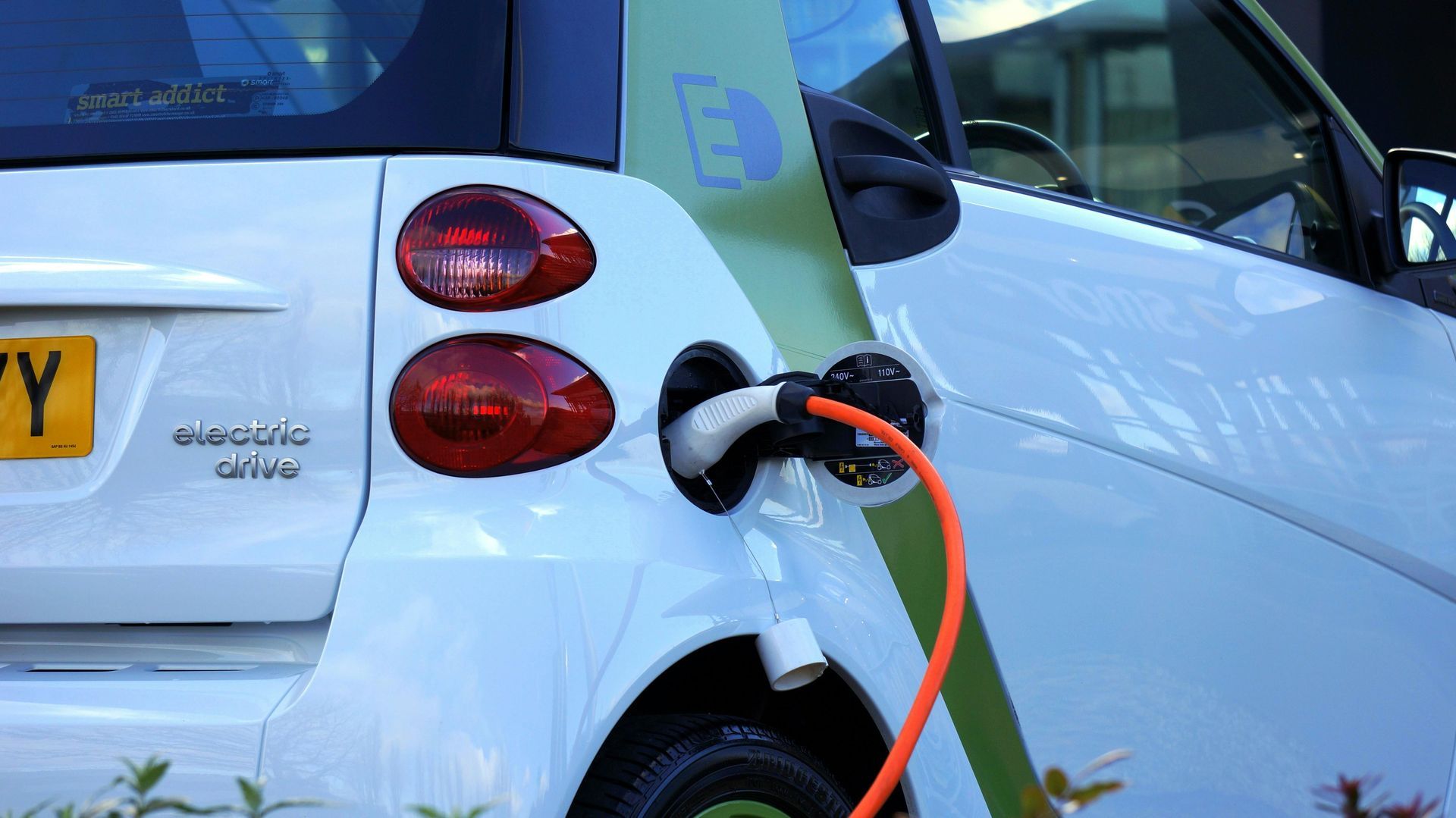 White electric car charging at a station. Orange charging cable plugged in.
